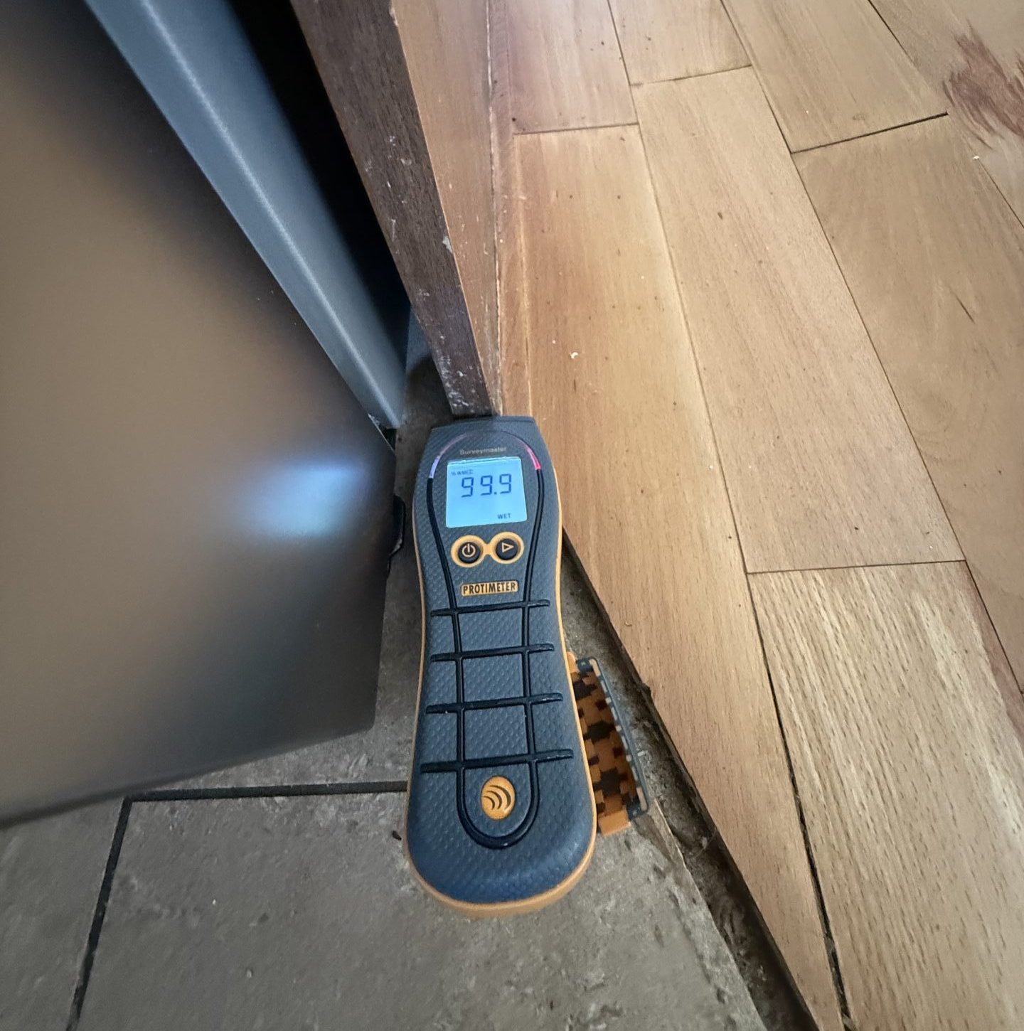 Professional moisture meter showing 99.9% excessive damp in a Limerick kitchen unit and timber floor during an insurance claim assessment.