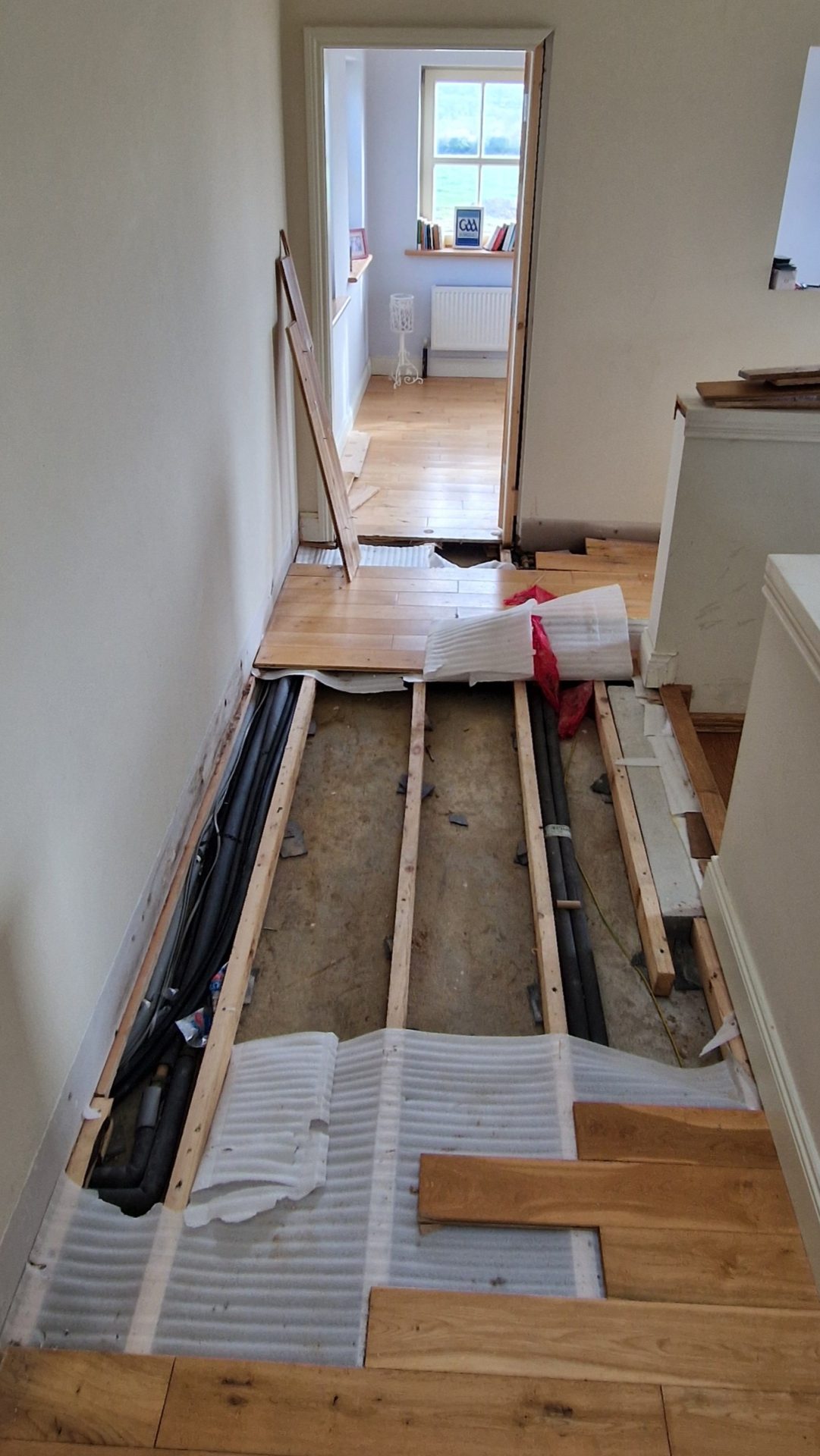 Torn up hardwood flooring exposing underfloor piping from a leak causing a boiler losing pressure in an Irish home.